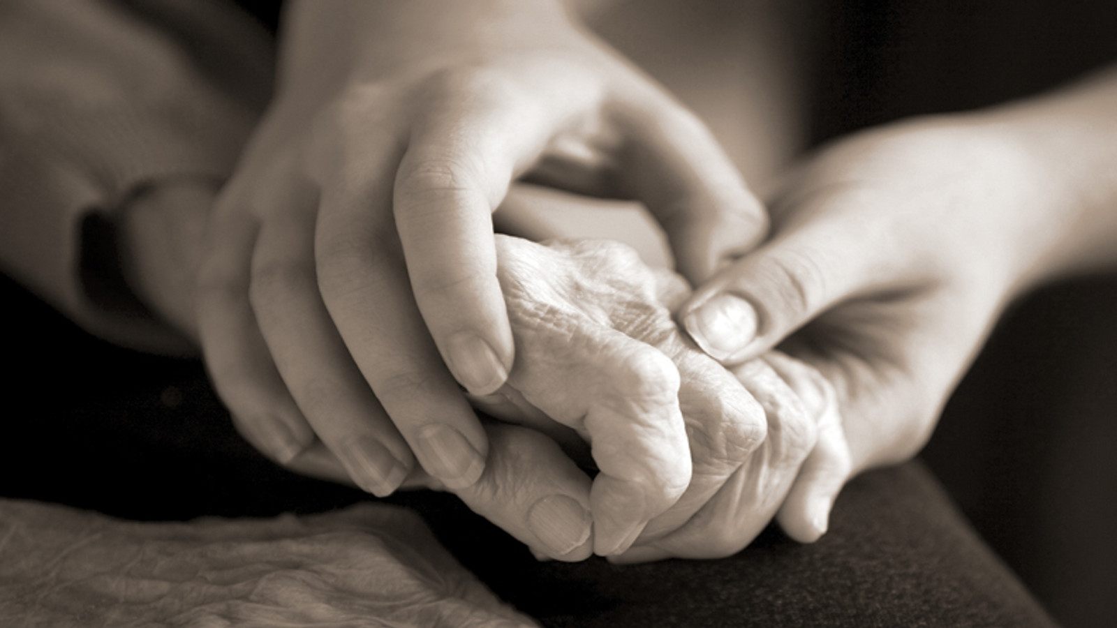 Mãos de uma pessoa idosa apoiadas por mãos cuidadoras